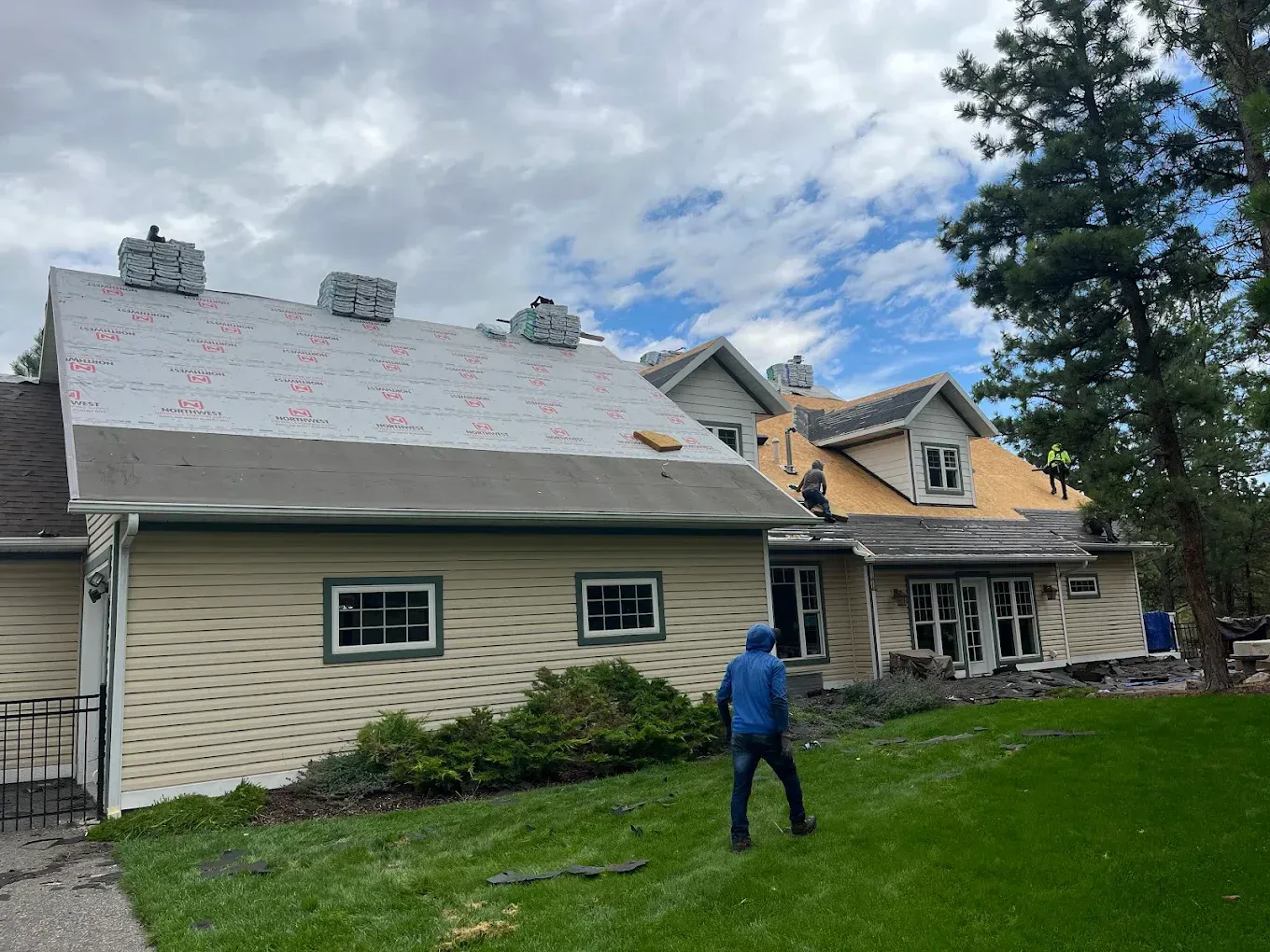 Roof being repaired; worker on lawn; partly completed roofing with two chimneys and green grass.