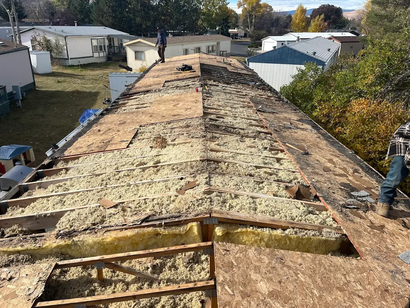 Mobile home roof partially stripped of shingles, revealing insulation and wooden supports.