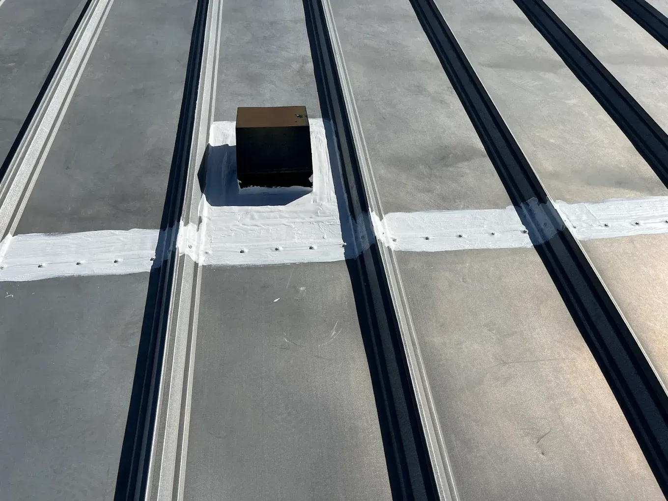 Gray metal roof with vent, sealed with white sealant.