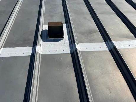 Gray metal roof with vent, sealed with white sealant.