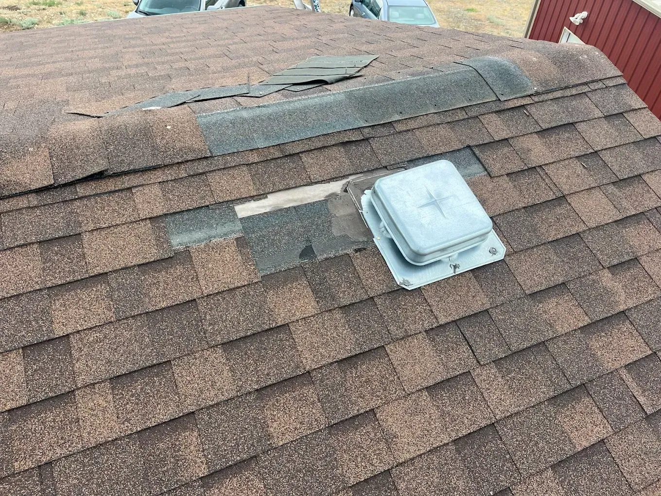 Damaged brown shingle roof with a vent; area around the vent is also damaged.