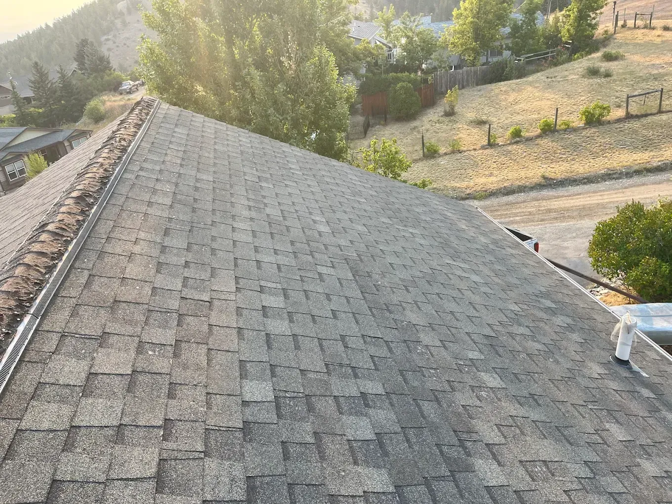 A sloped roof covered in gray shingles, with a valley gutter and trees in the background.