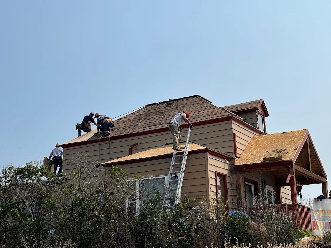 Roofers installing shingles on a two-story house under a blue sky.