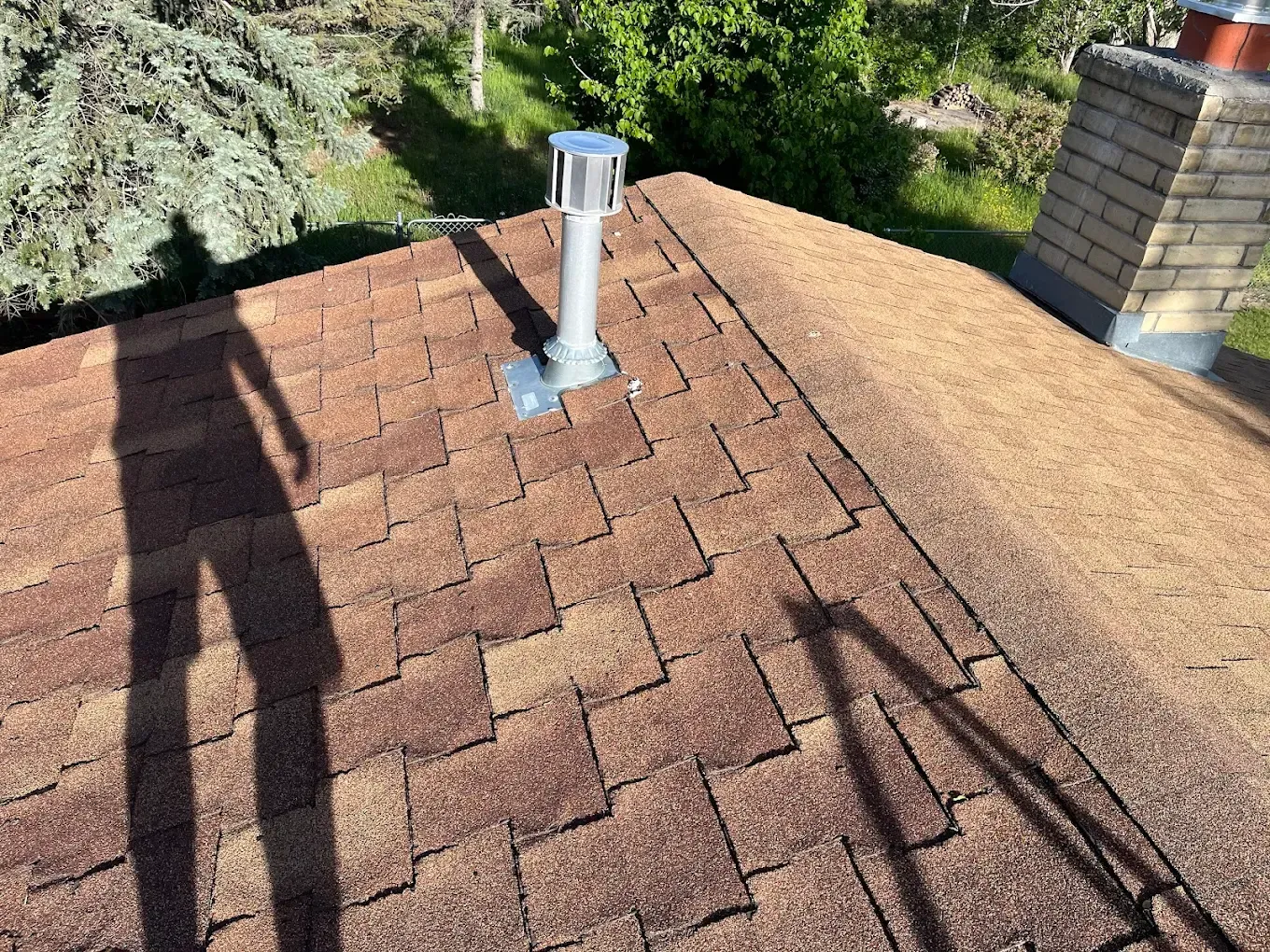 Brown roof with vent pipe, shadow of a person standing.