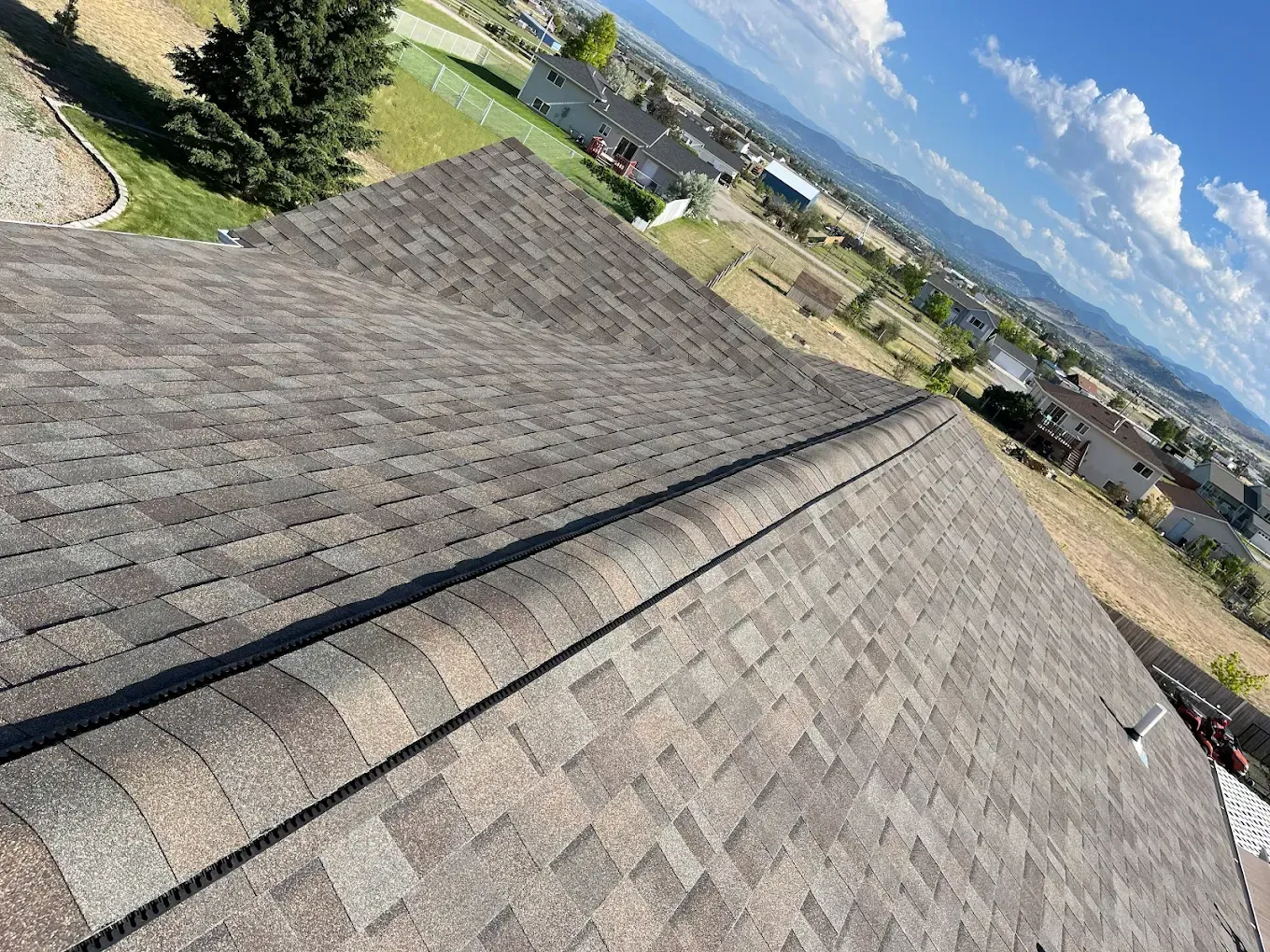 Brown asphalt shingle roof with a valley, a clear sky and a residential landscape.
