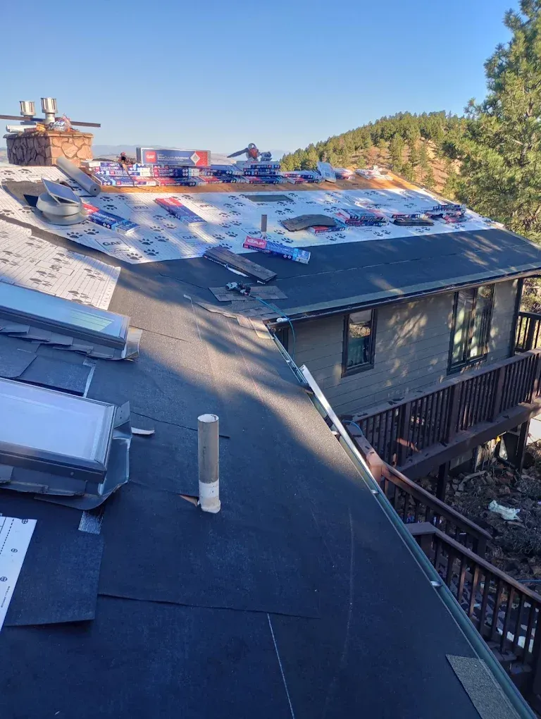 Roof replacement in progress on a house. Blue sky, shingles, and tar paper visible.