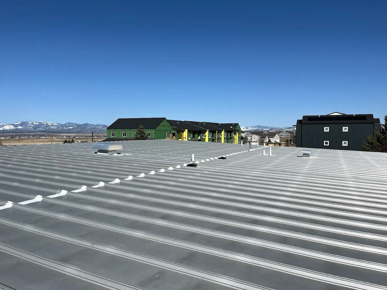 Metal roof with a cityscape in the background under a clear, blue sky.
