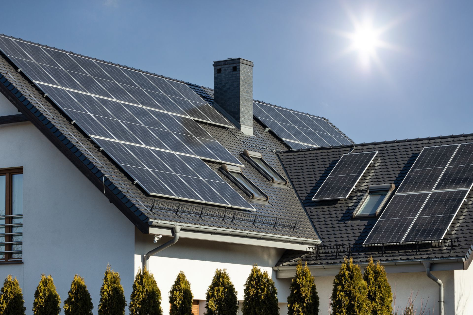 A house with dark solar panels installed across its roof under a bright, sunny sky.