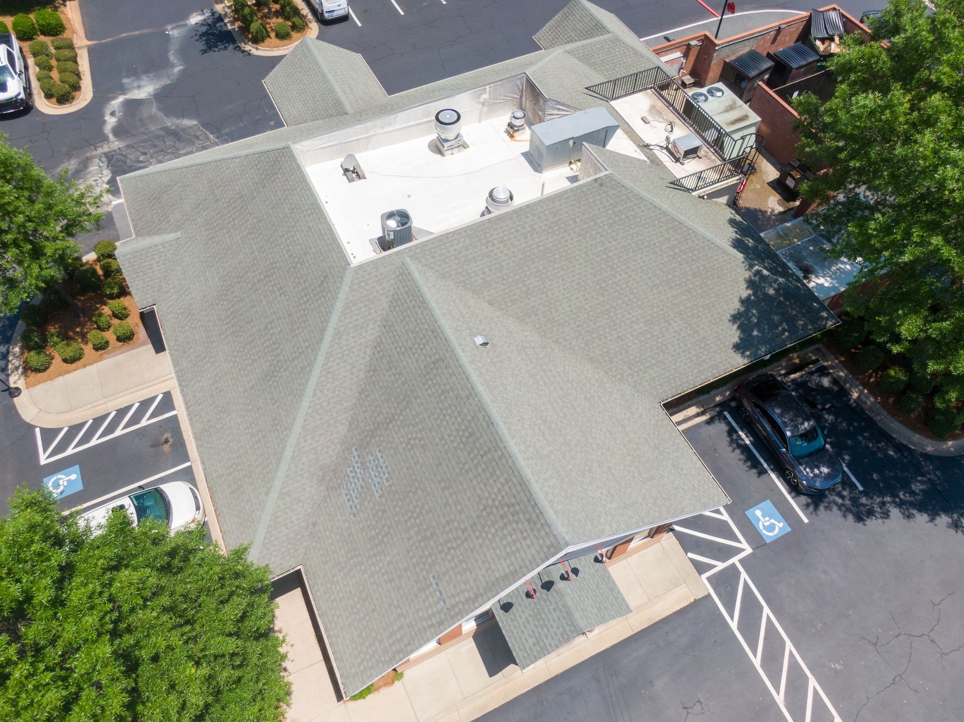 Two workers in safety gear and hard hats kneeling on a metal roof, securing panels with a power tool.