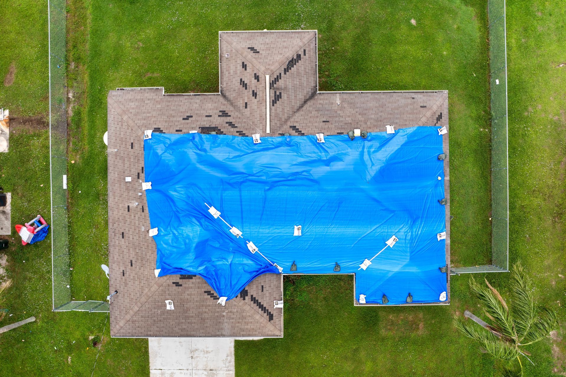 An aerial view of a house with a large blue tarp covering a significant portion of its brown shingled roof.