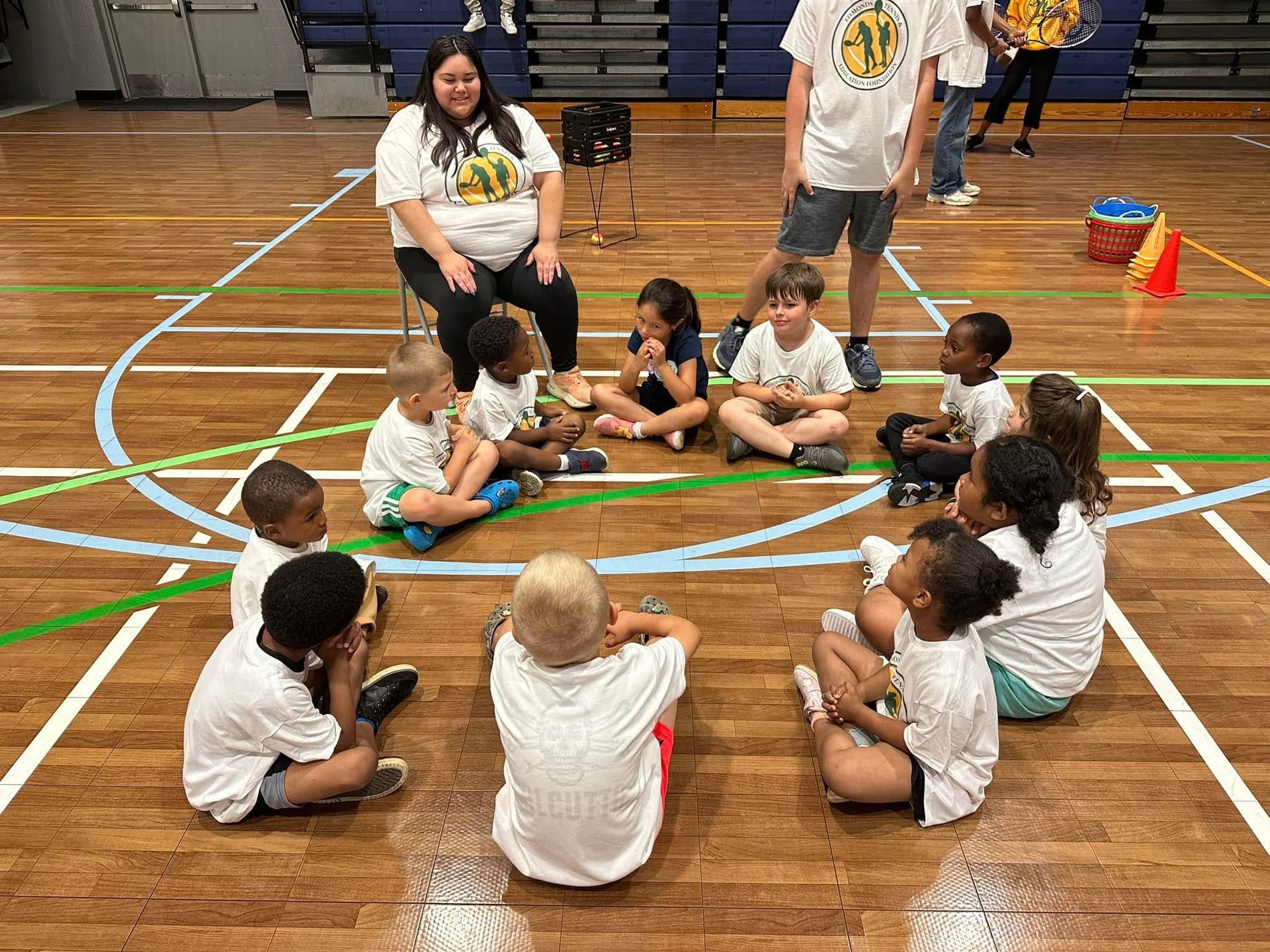 A group of children are sitting in a circle on a basketball court.