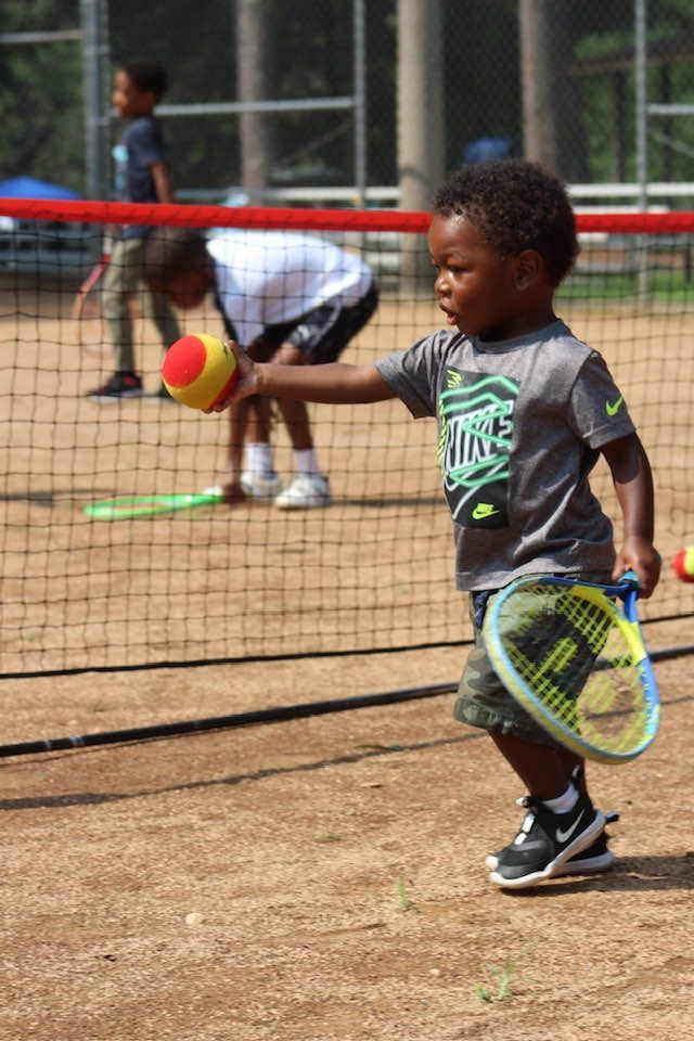 A young boy is holding a tennis racquet and a tennis ball.