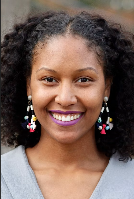 A woman with curly hair and glasses is smiling for the camera