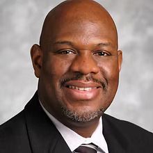 A bald man in a suit and tie is smiling for the camera.