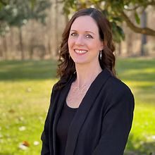 A woman in a black jacket is smiling for the camera in a park.