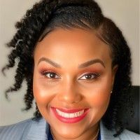 A woman with curly hair is smiling and wearing a suit.