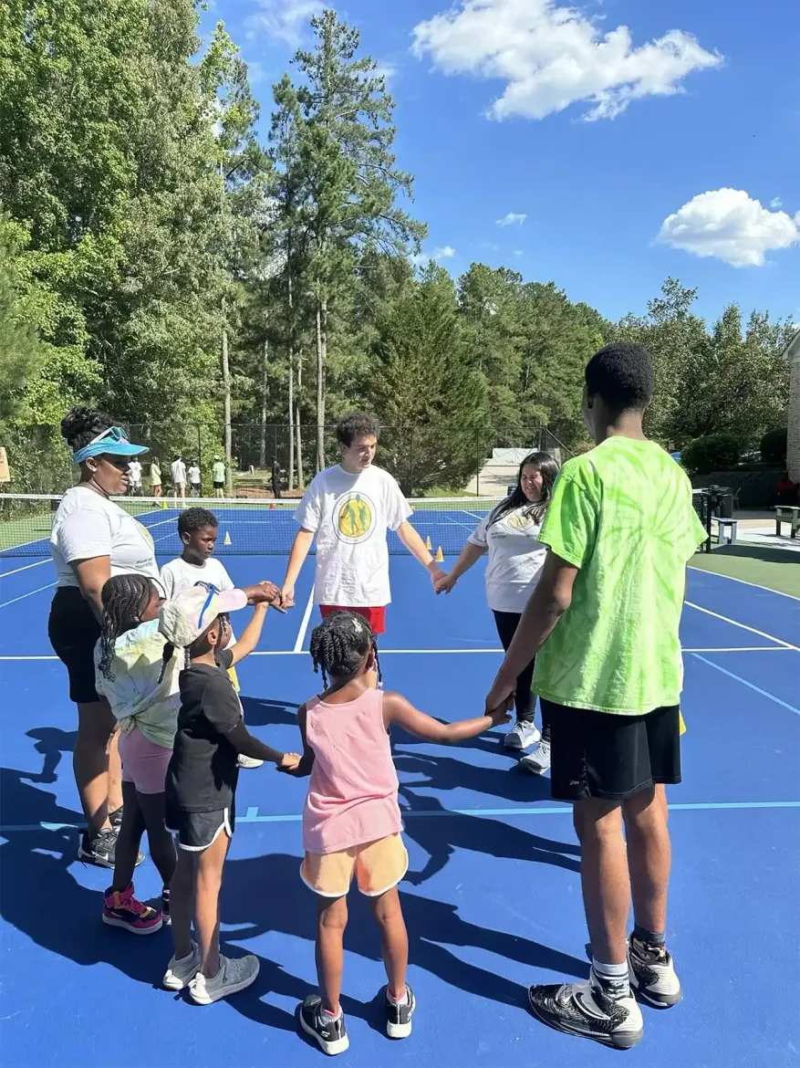 A group of people are standing on a tennis court holding hands.