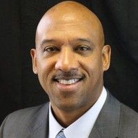 A bald man in a suit and tie is smiling for the camera.