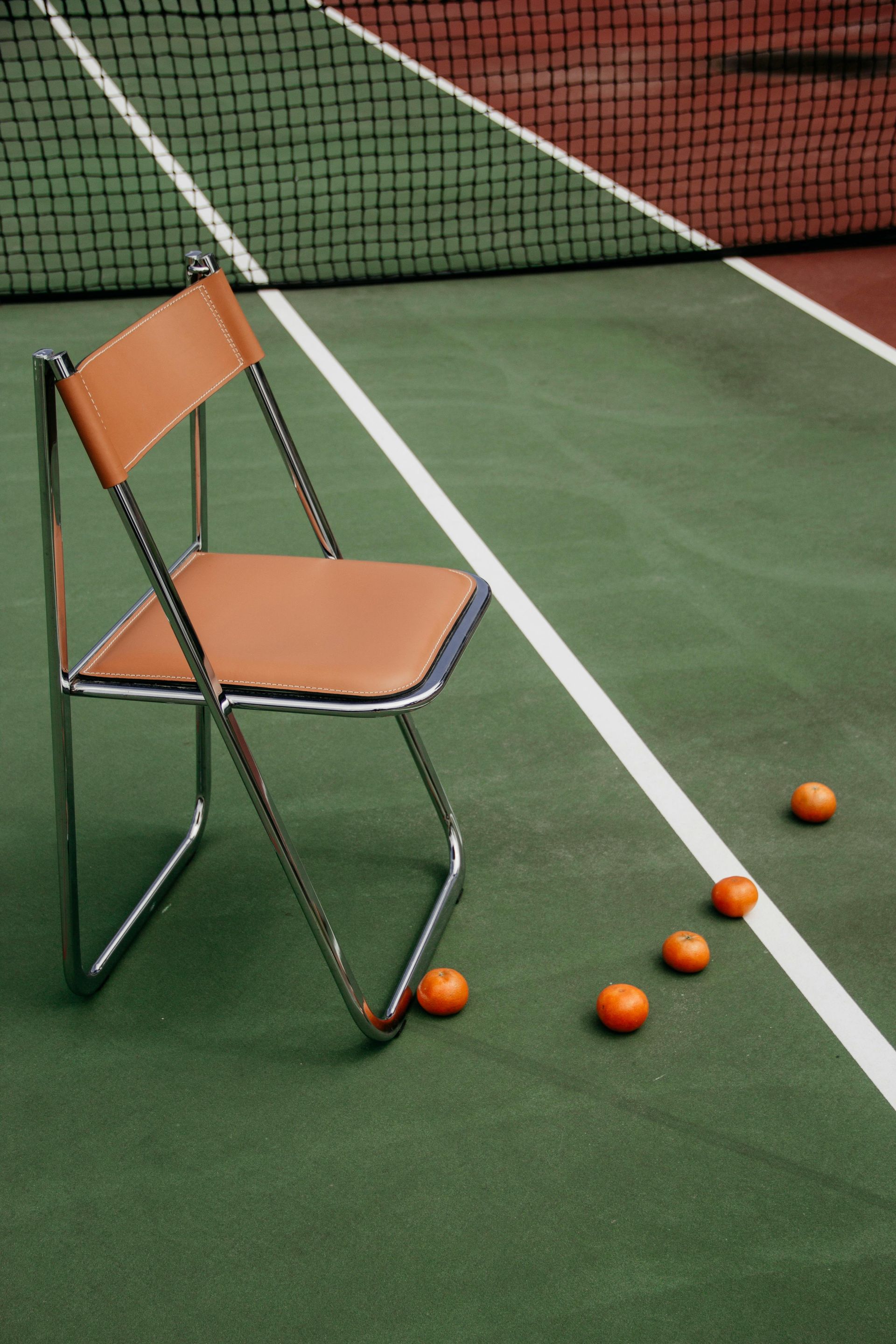 A chair sits on a tennis court next to oranges