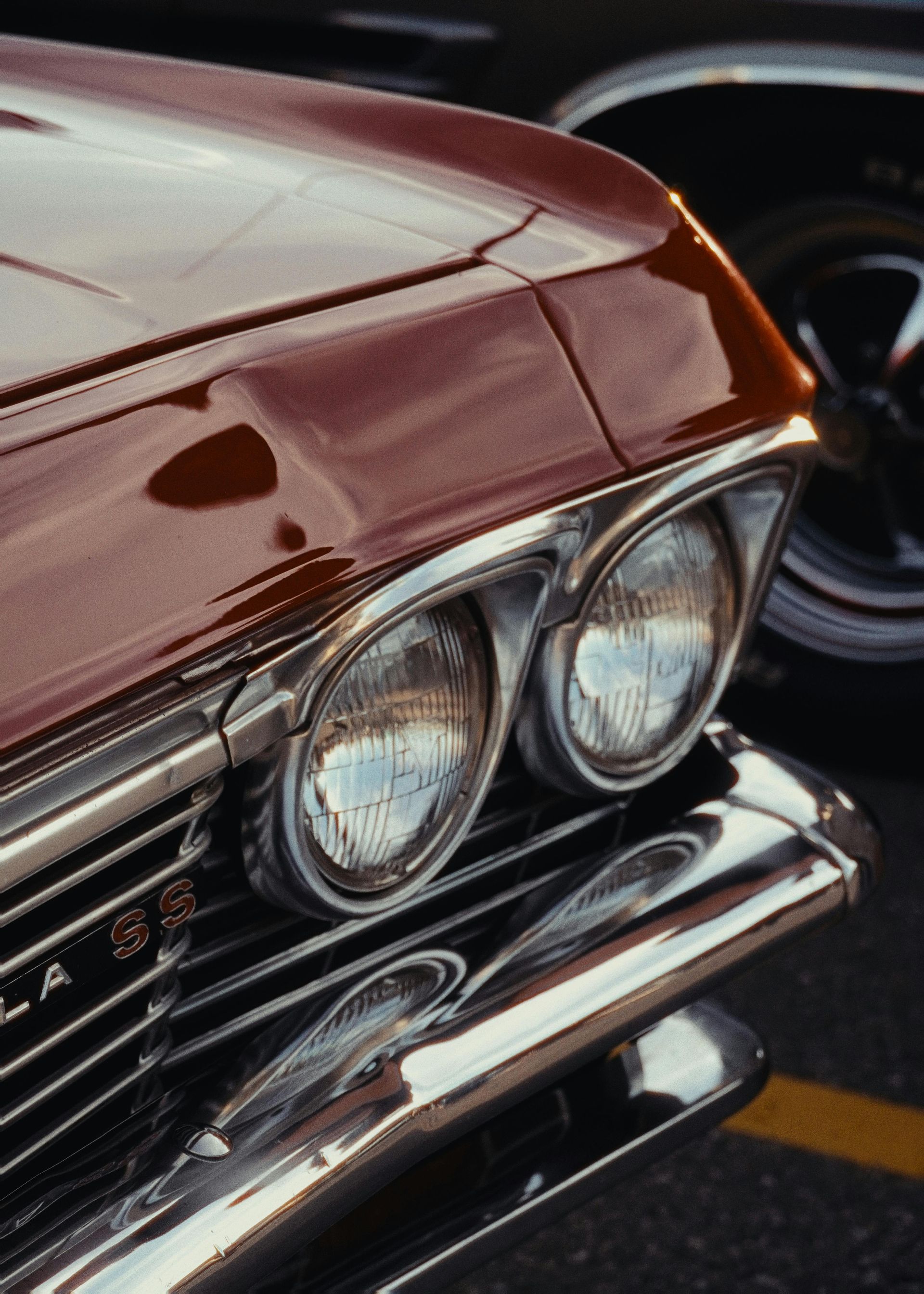 Red vintage car's front with dual headlights, chrome trim, and partial view of a tire.