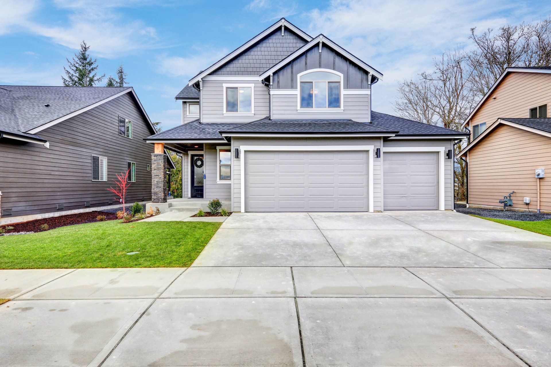 A large gray house with a concrete driveway in front of it.