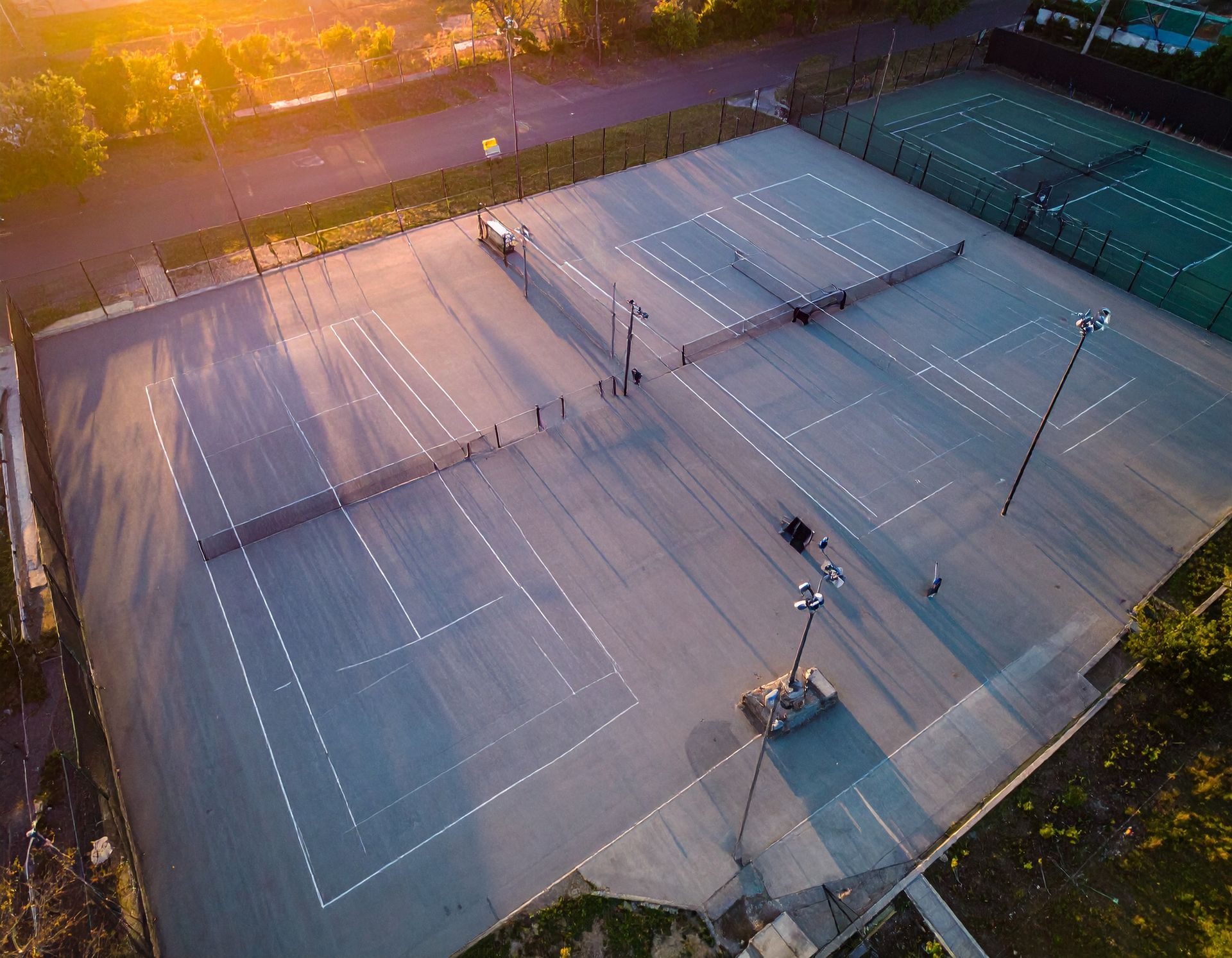 Aerial view of tennis courts with players, lit by sunset.