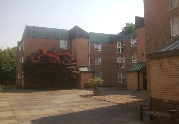 Brick building with multiple floors, dark roof, courtyard, and a red-leafed tree.