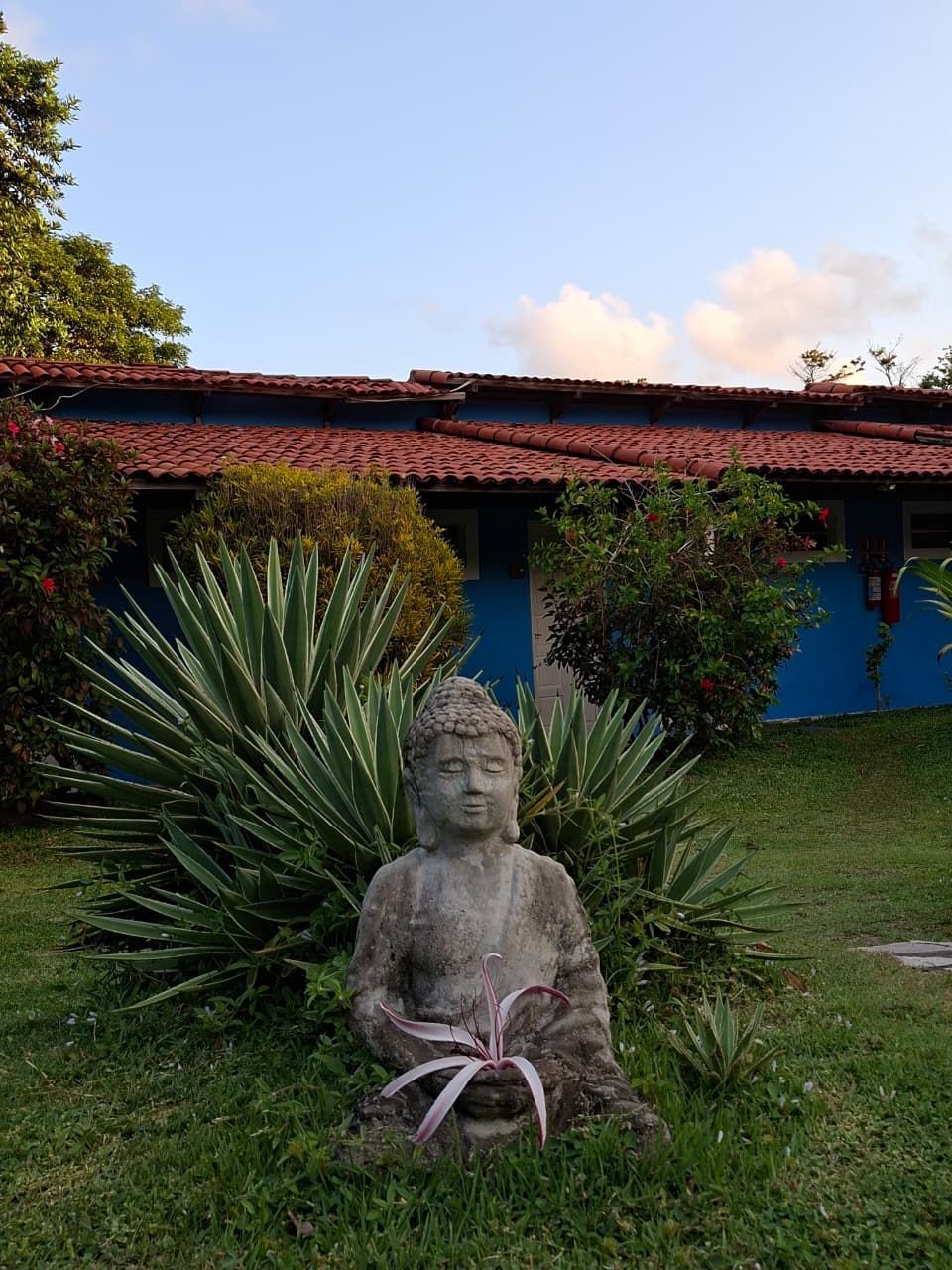 Estátua de Buda de pedra em um gramado em frente a um prédio azul com telhado vermelho.