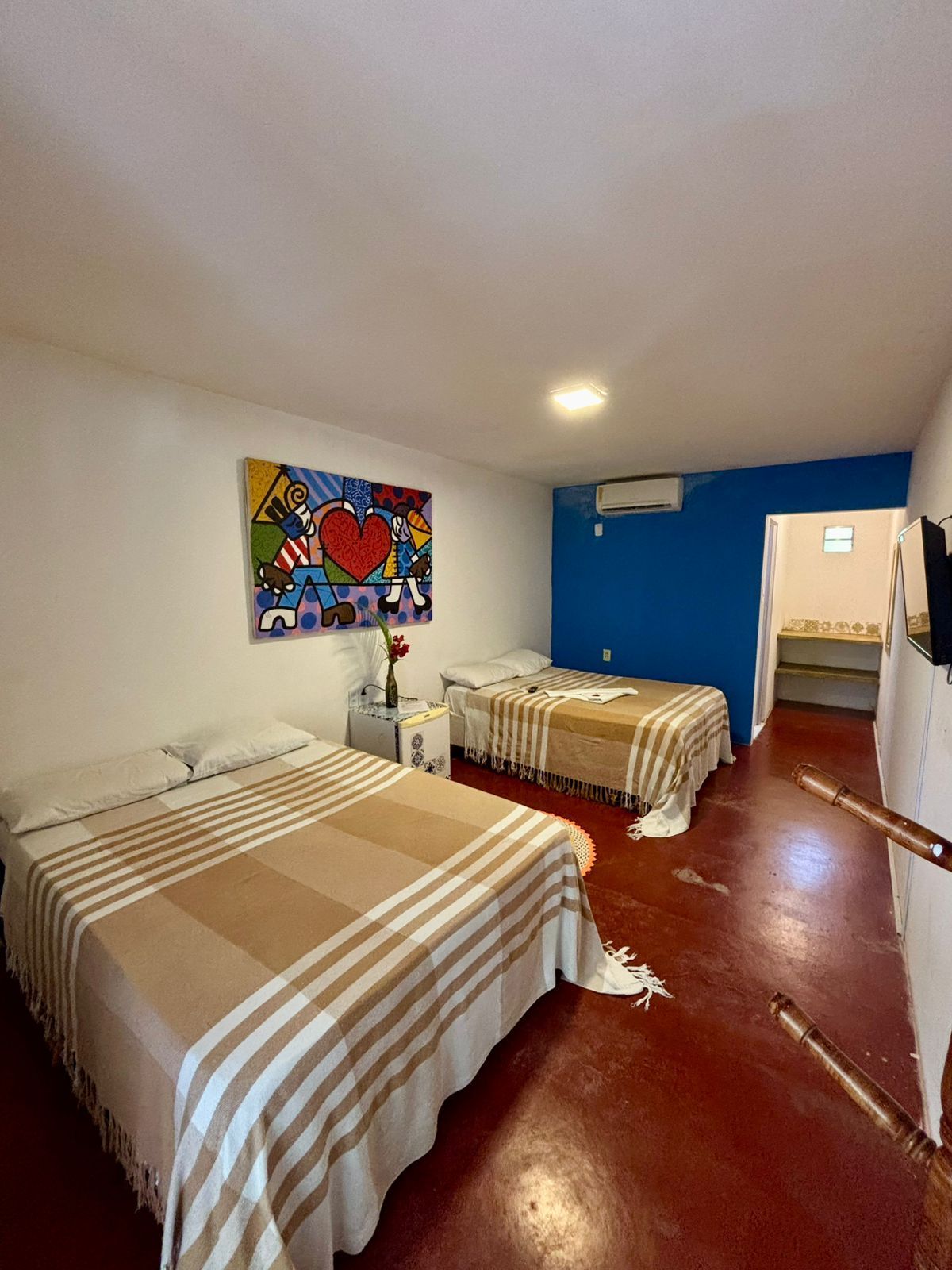 Quarto com duas camas, piso vermelho, parede azul, obras de arte.