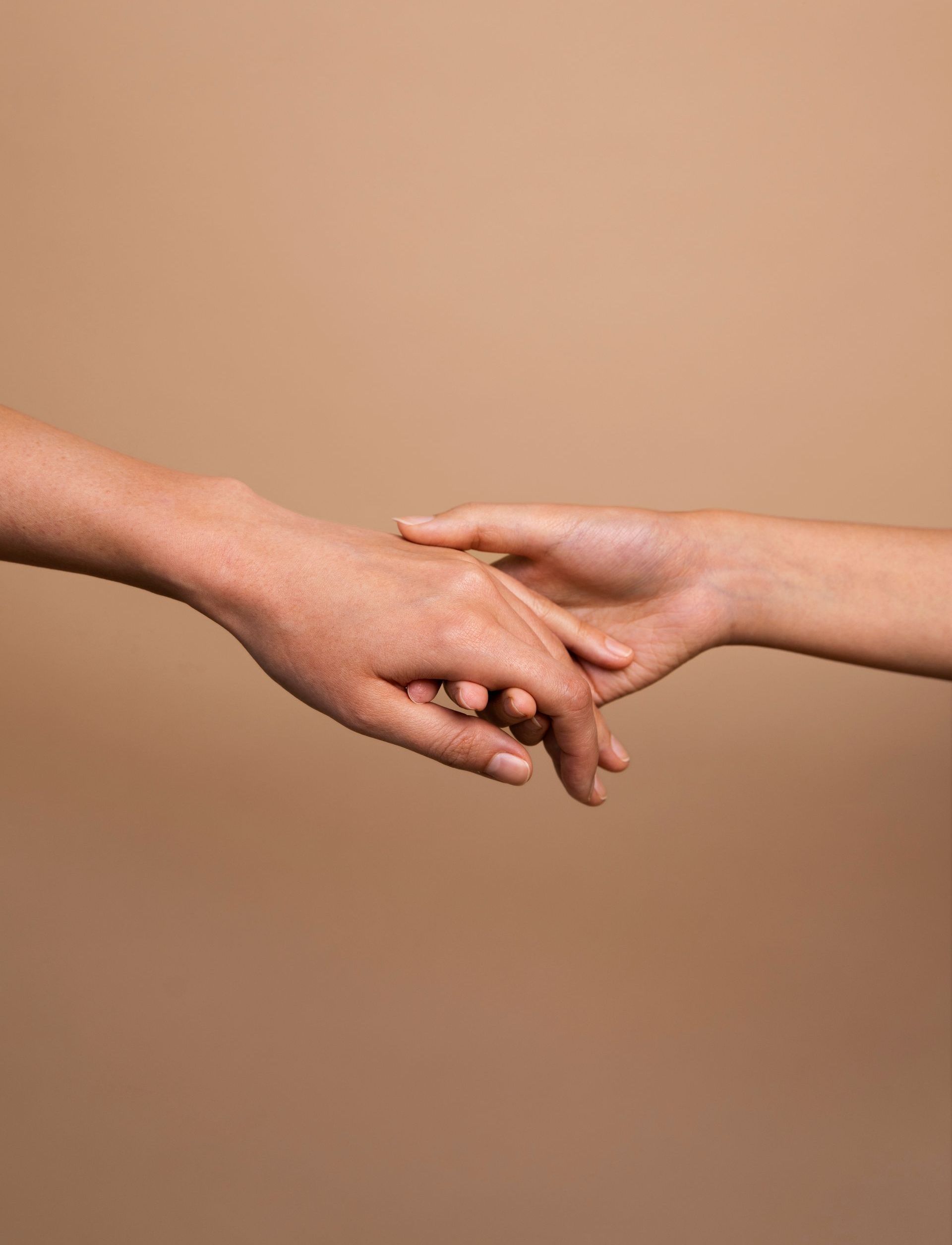 Un hombre y una mujer se toman de la mano sobre un fondo marrón.