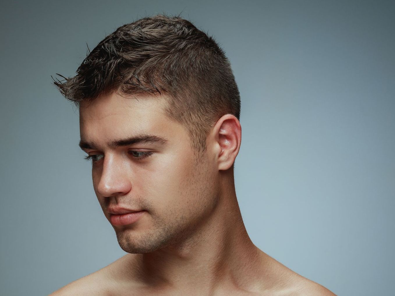 Un joven sin camisa y con la cabeza rapada mira hacia abajo.