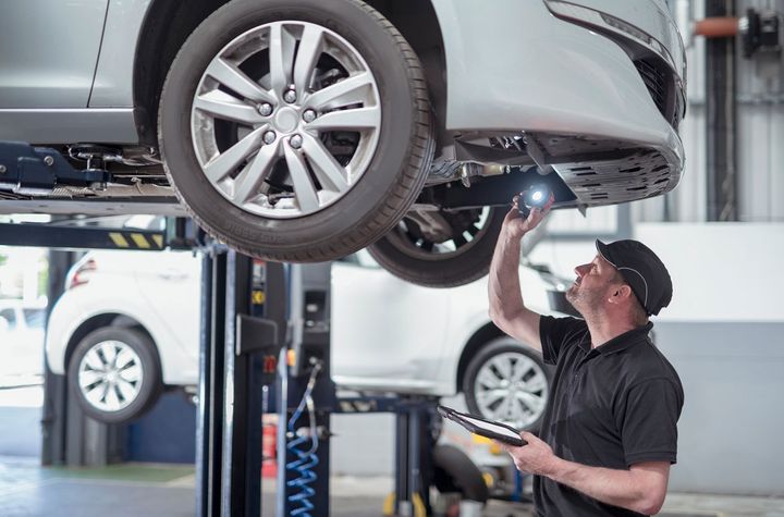 A man is working on a car on a lift in a garage.