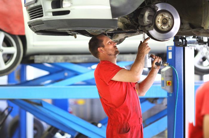 A man is working under a car on a lift in a garage.