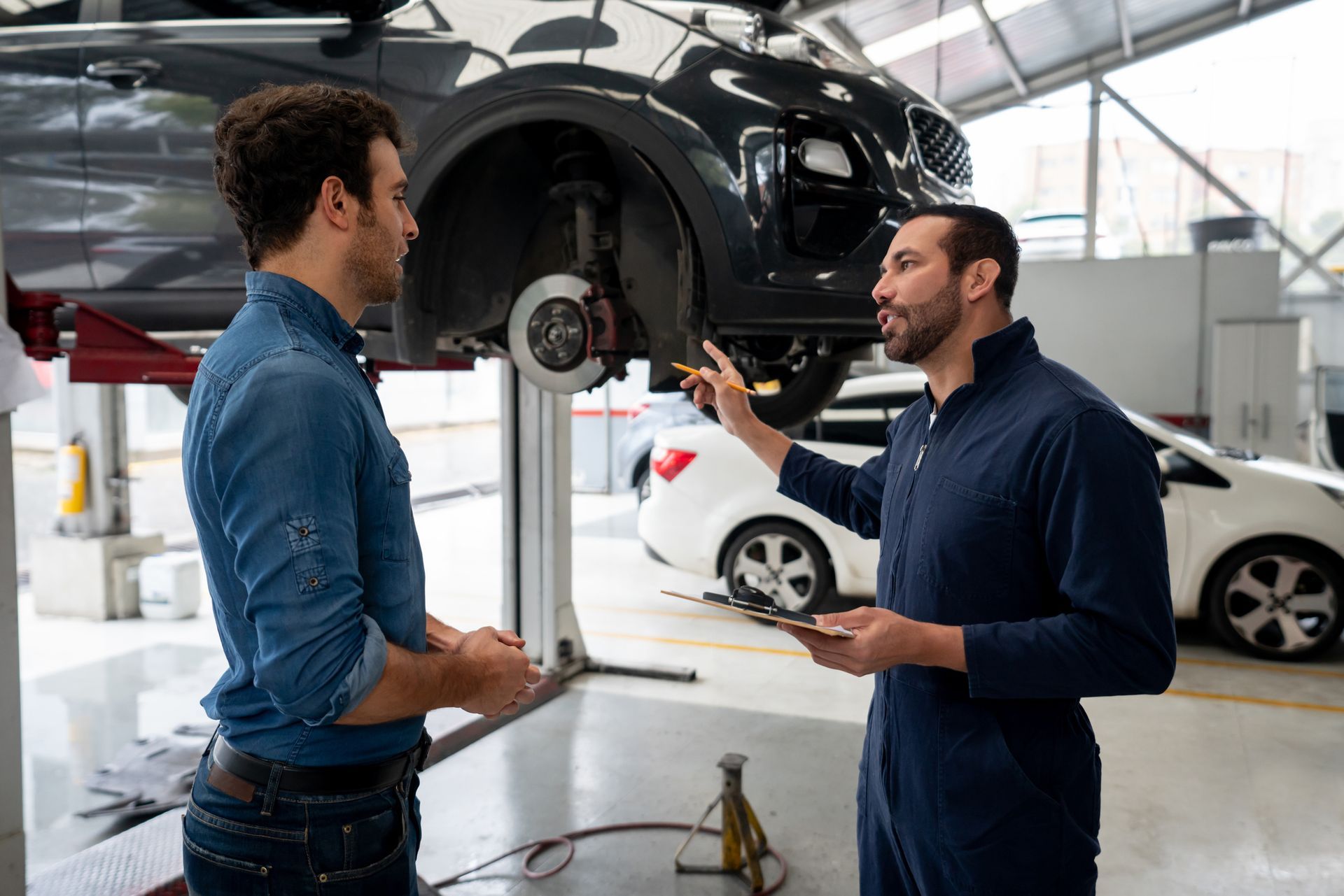 Mechanic talks to customer at brake shop while inspecting car in professional auto repair garage. Mechanic talks to customer at brake shop while inspecting car in professional auto repair garage.