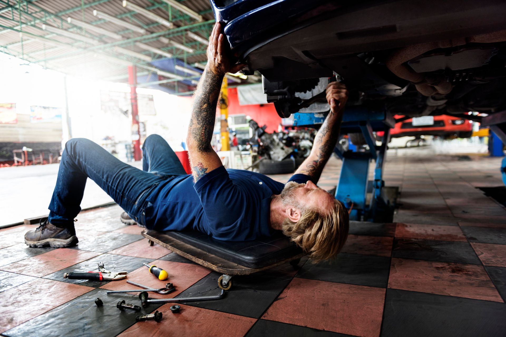 A mechanic is working under a car at a brake repair shop, performing brake repairs on the vehicle.