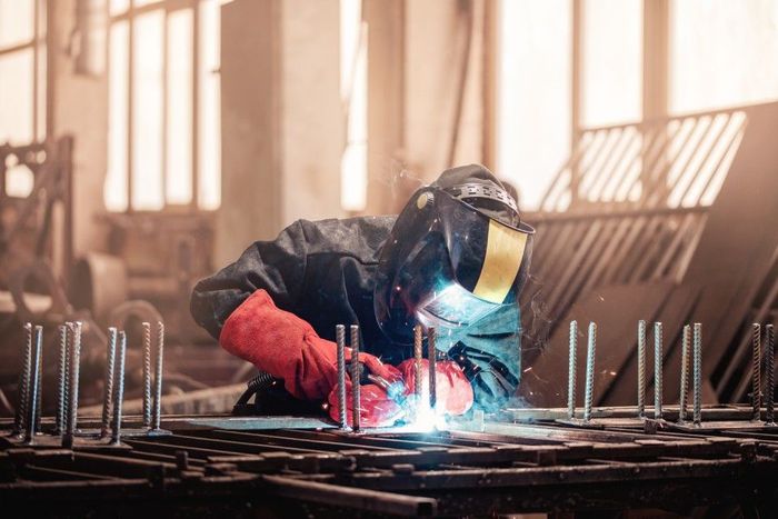 man is welding a piece of metal in a factory.