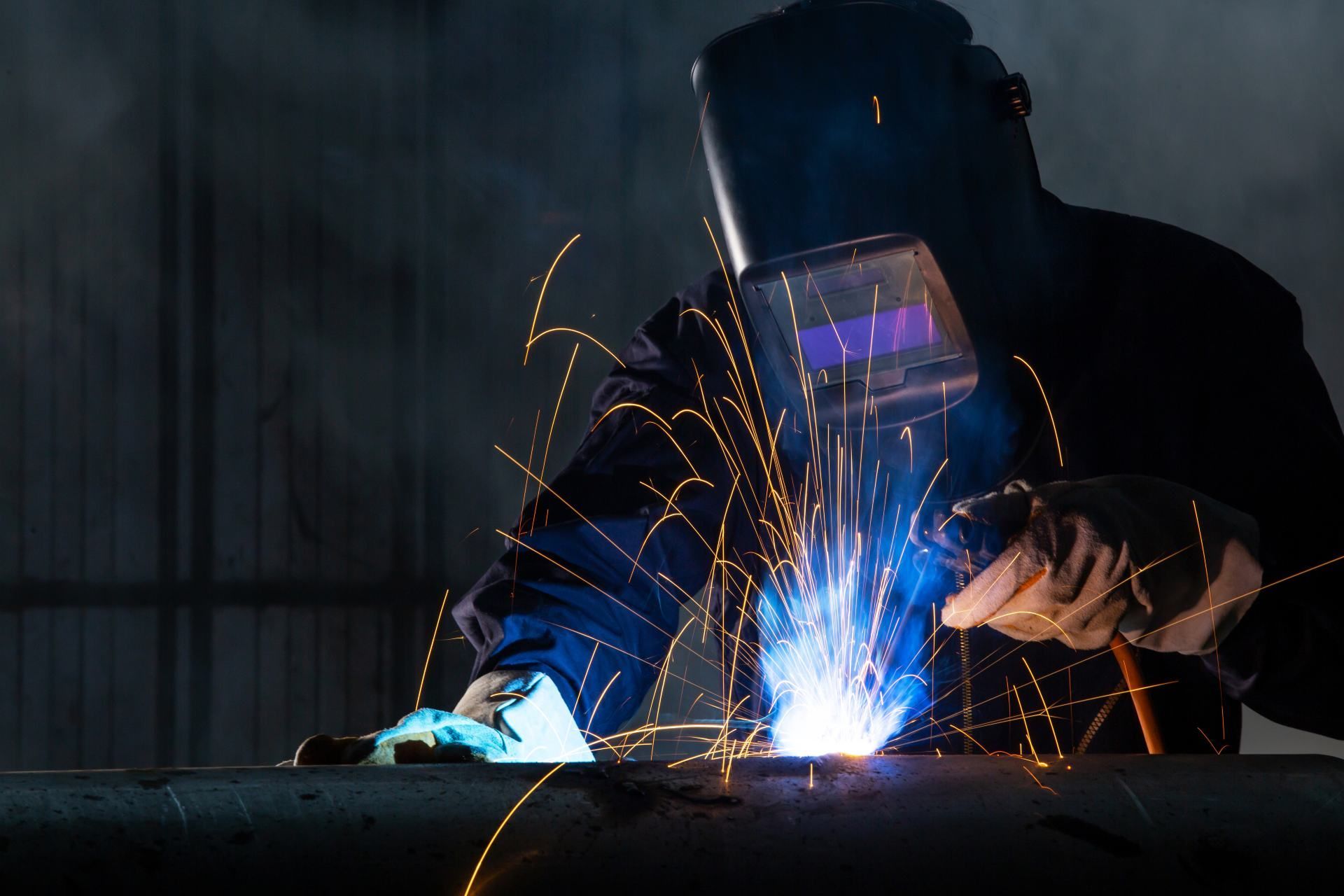 A man wearing a welding mask is welding a piece of metal.