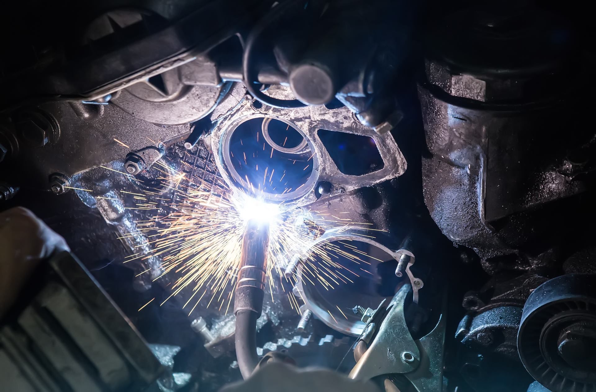 person is welding a pipe under a car.