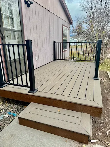 A small, elevated deck with taupe composite flooring, black metal railings, and a single step leading to a concrete base.