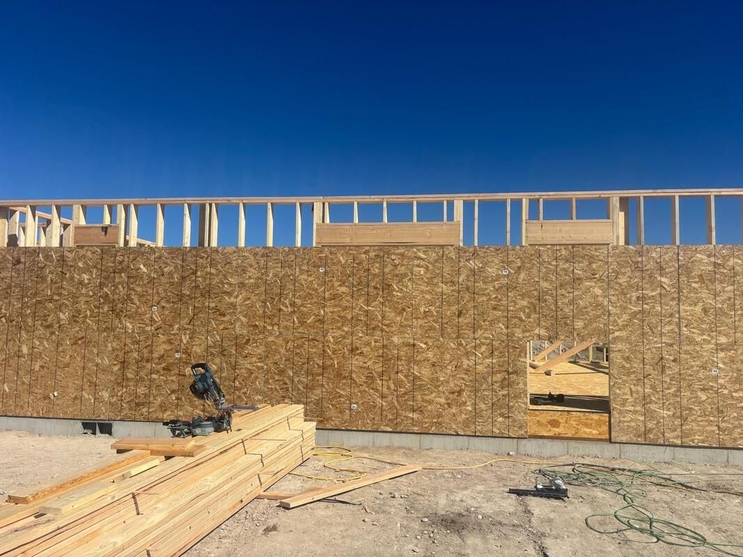 Framed wall under construction with plywood sheathing, exposed top studs, and a doorway opening on a dirt lot.