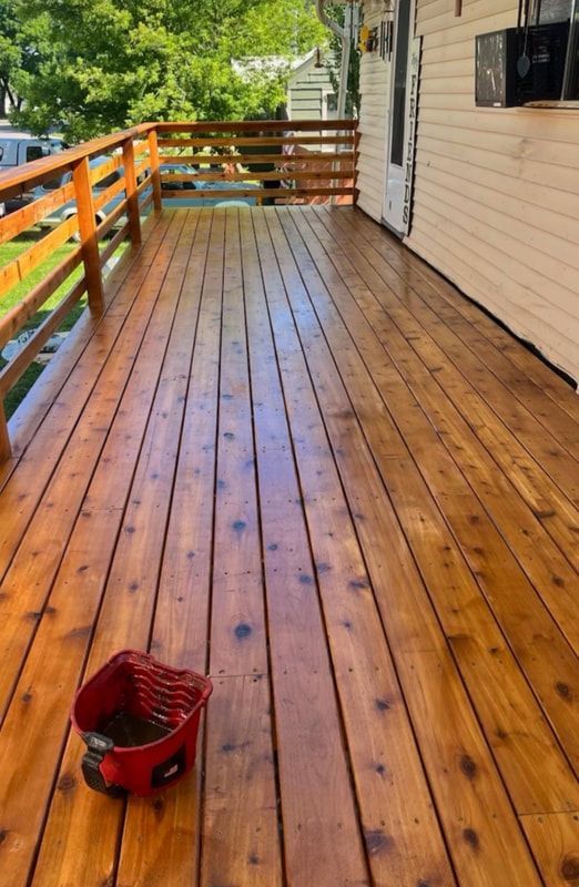 A freshly stained, glossy wooden deck with a wooden railing and a small red paint bucket sitting on the floorboards.