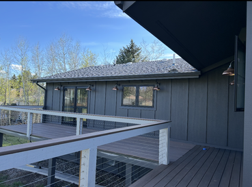A dark gray modern house exterior with vertical siding and a spacious wooden deck featuring a cable railing.