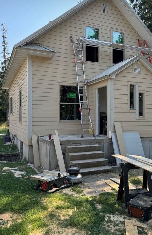 A house under construction with beige siding, a metal ladder against the wall, new windows, and a front concrete porch.