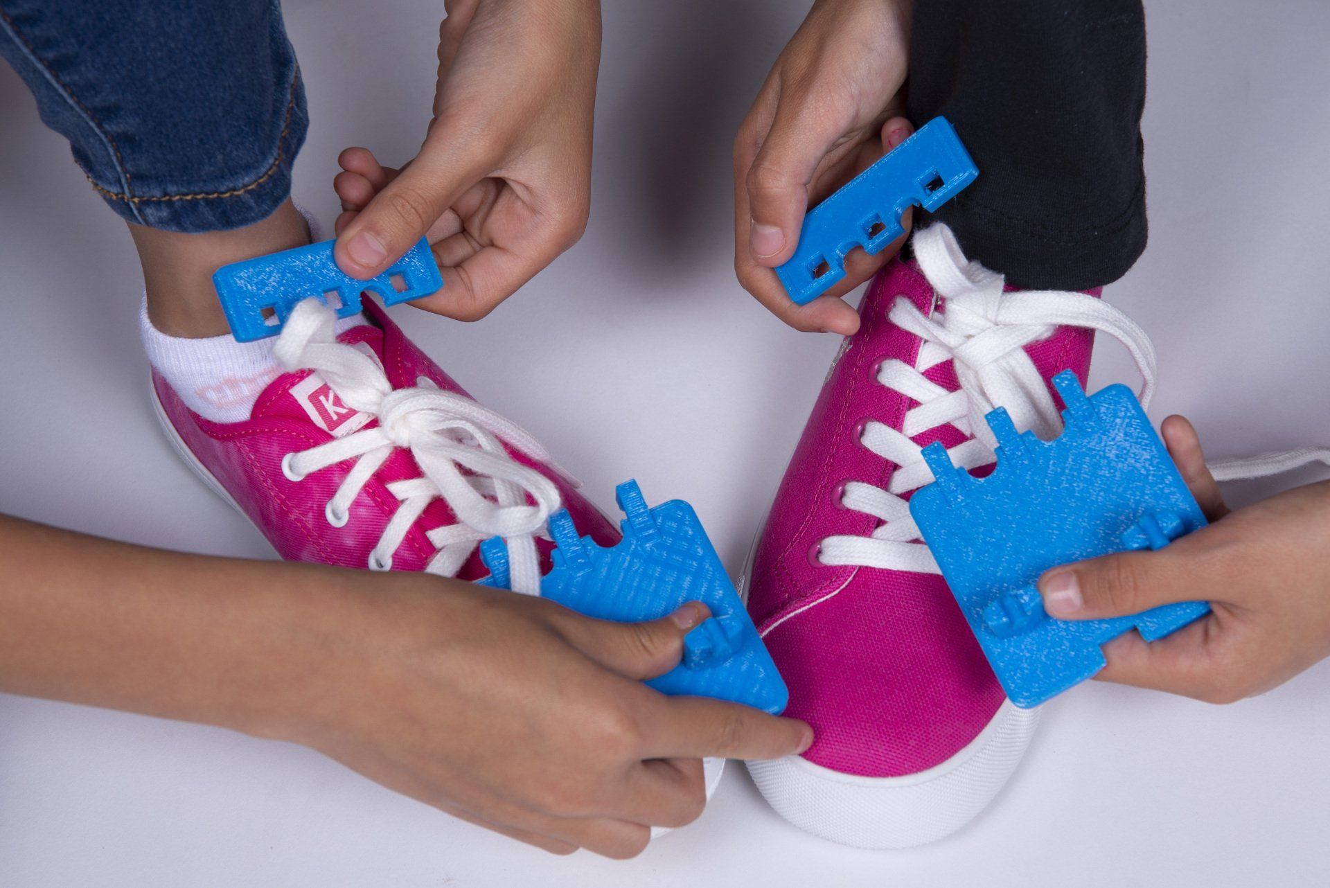 A person is tying a pair of pink sneakers with blue laces.