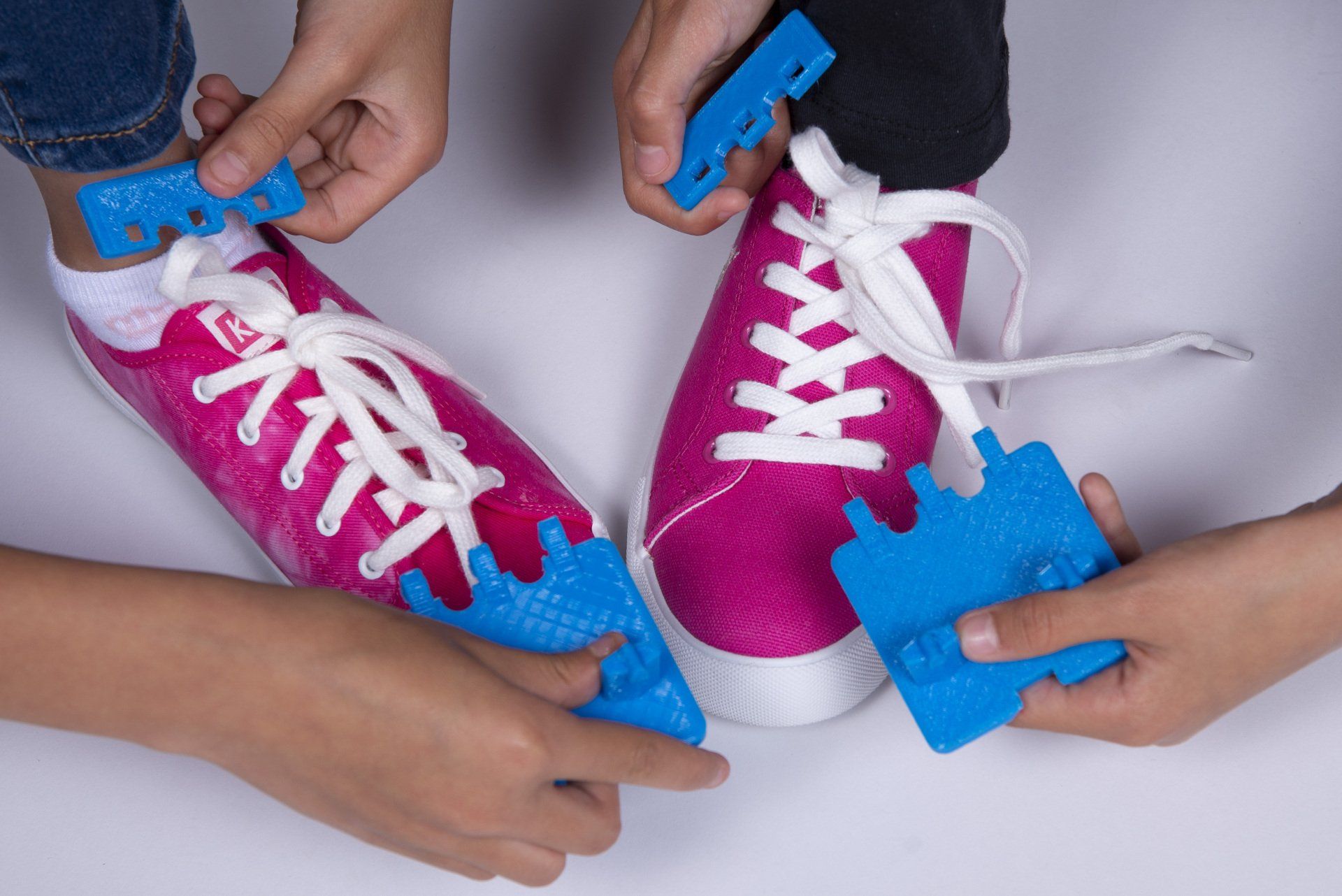 A person is tying a pair of pink sneakers with blue laces