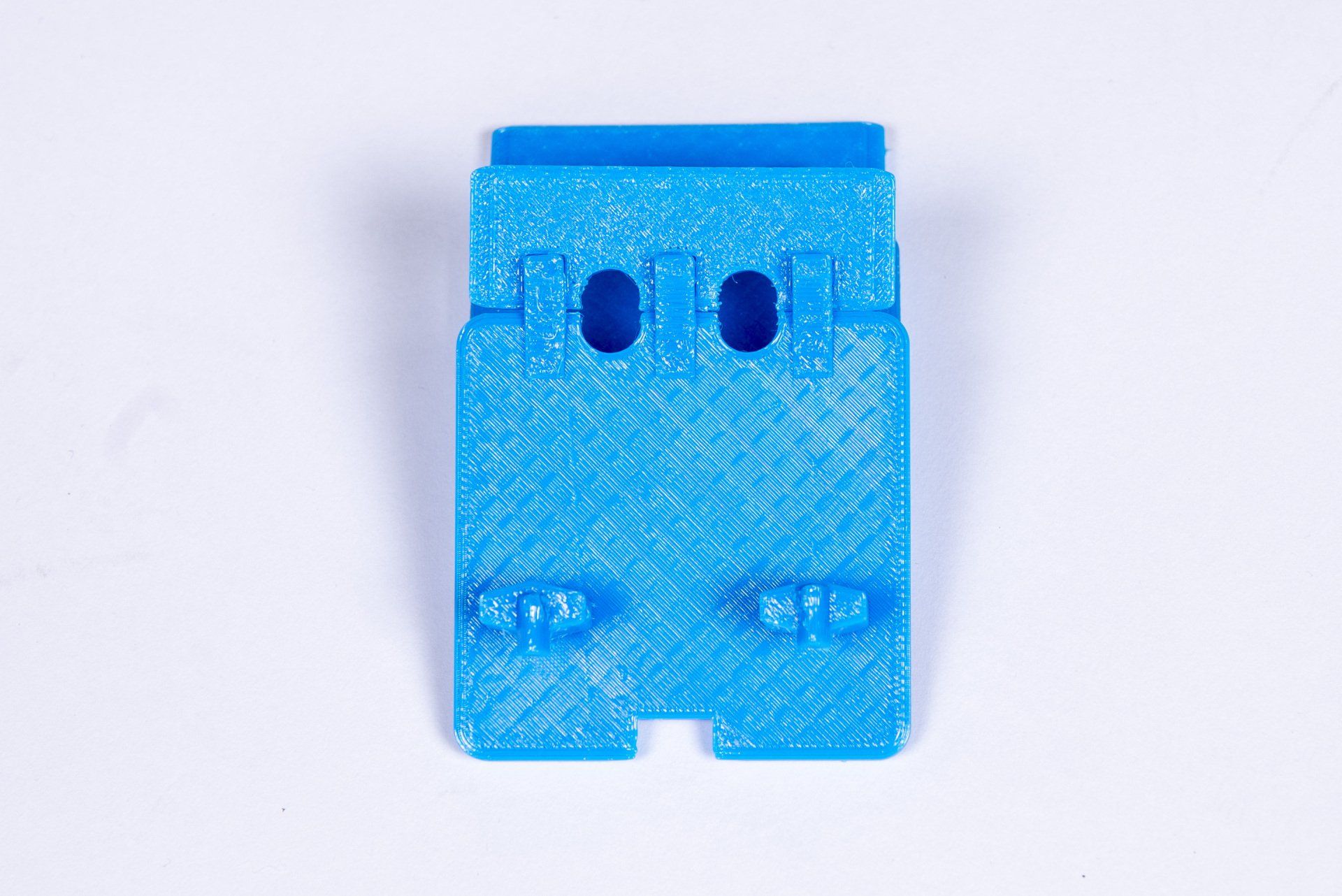 A blue plastic object with two holes in it is sitting on a white surface.