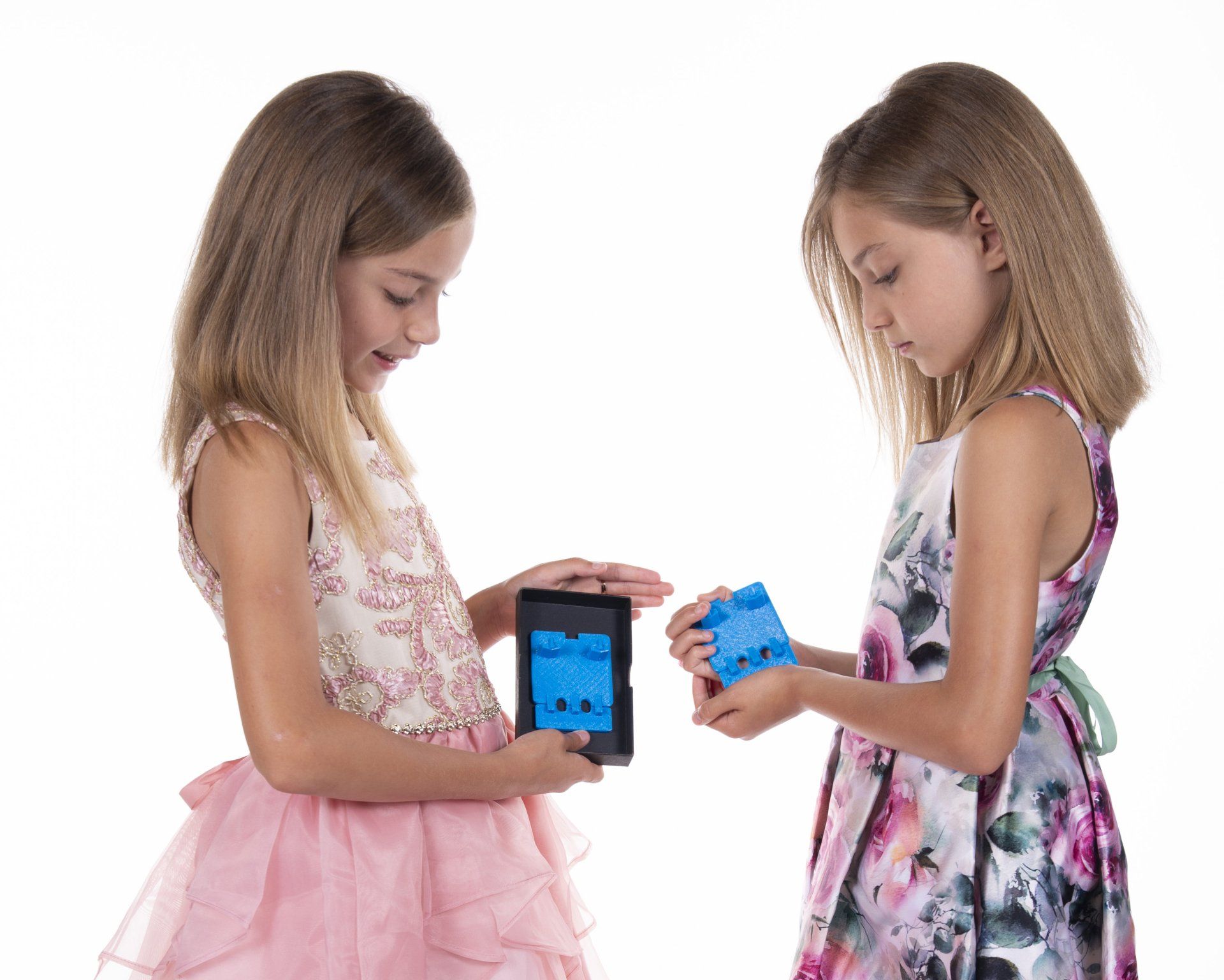 Two young girls are playing with a tablet and a blue cube.