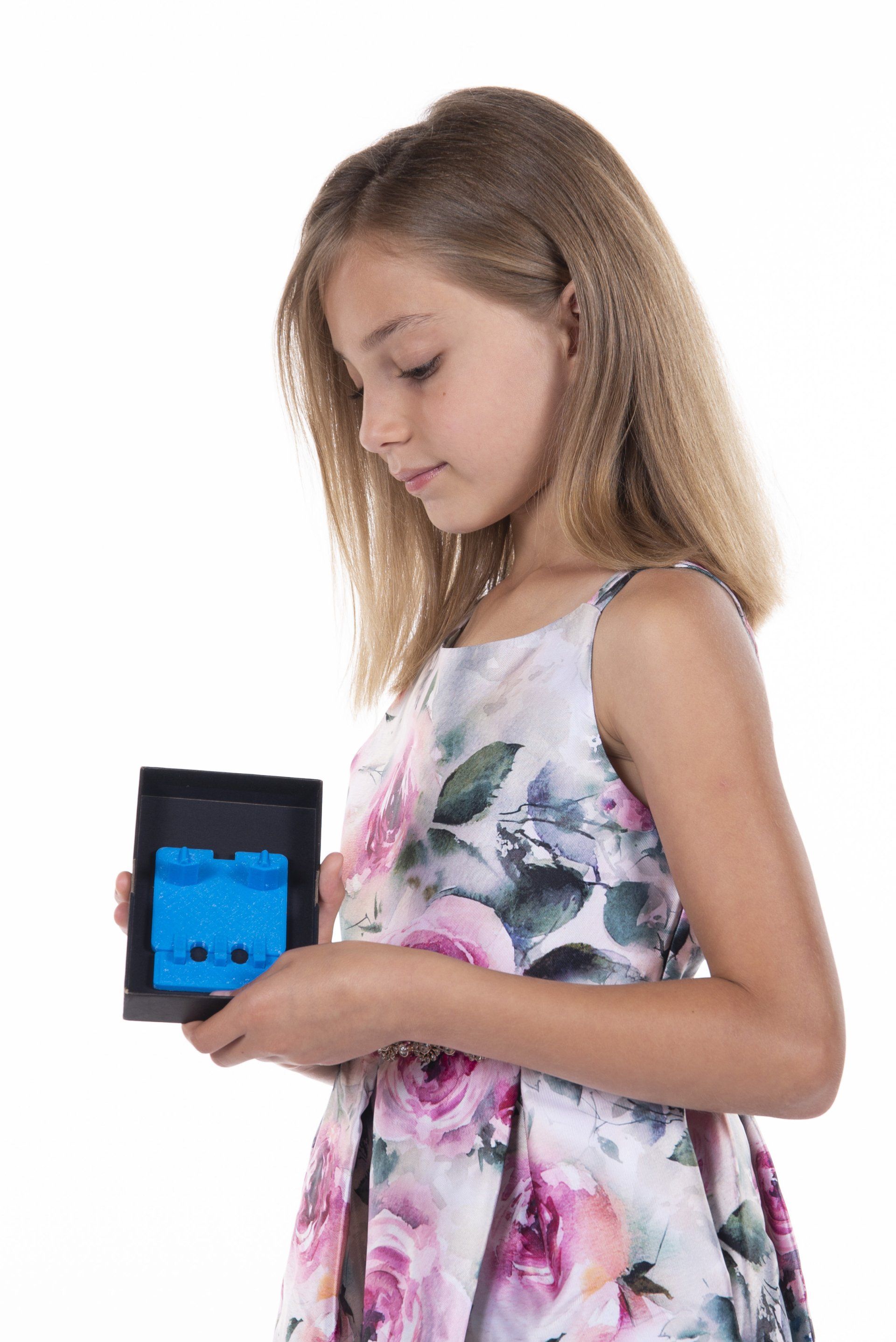A young girl in a floral dress is holding a blue box.