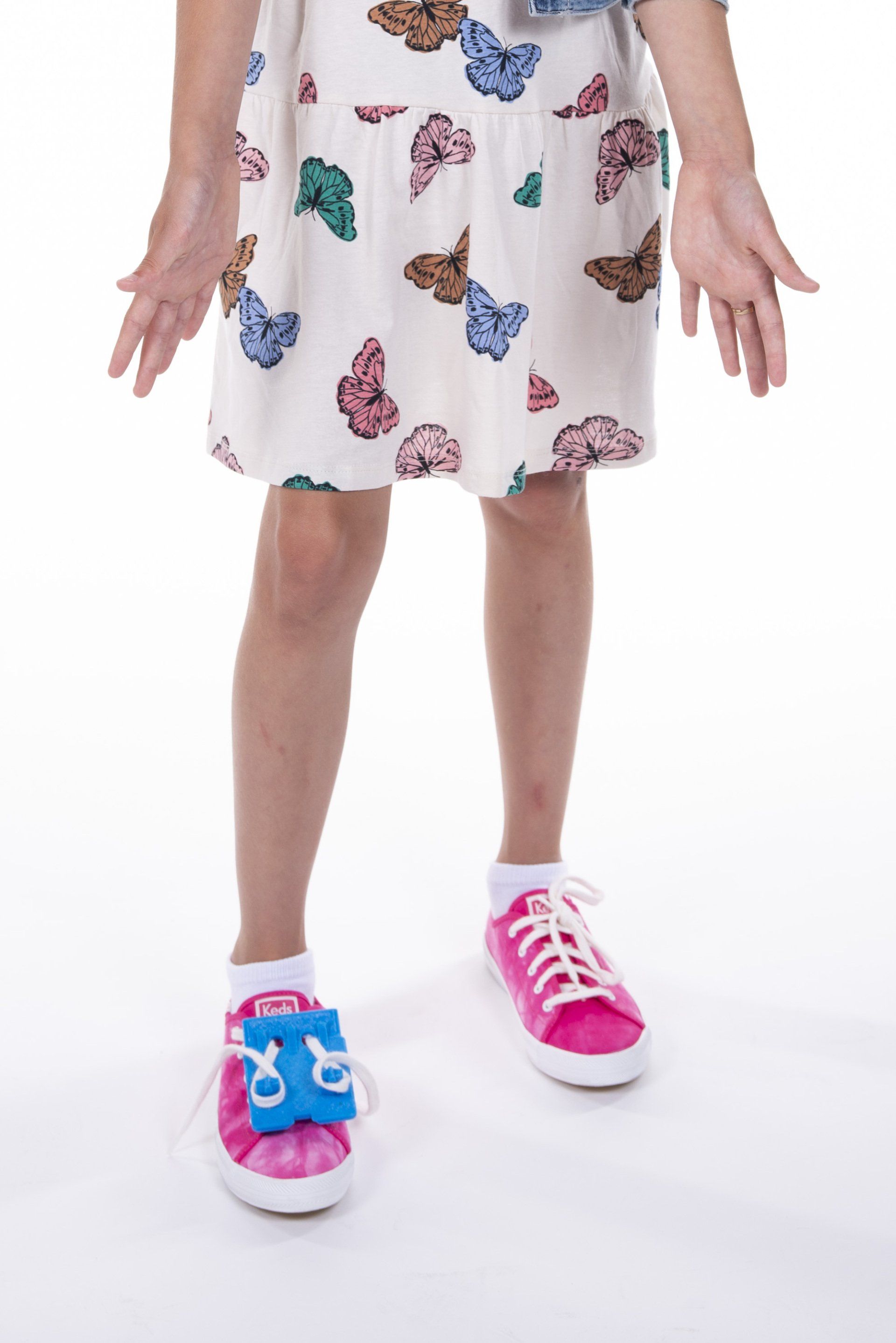 A little girl is wearing a white skirt with butterflies on it and pink sneakers.