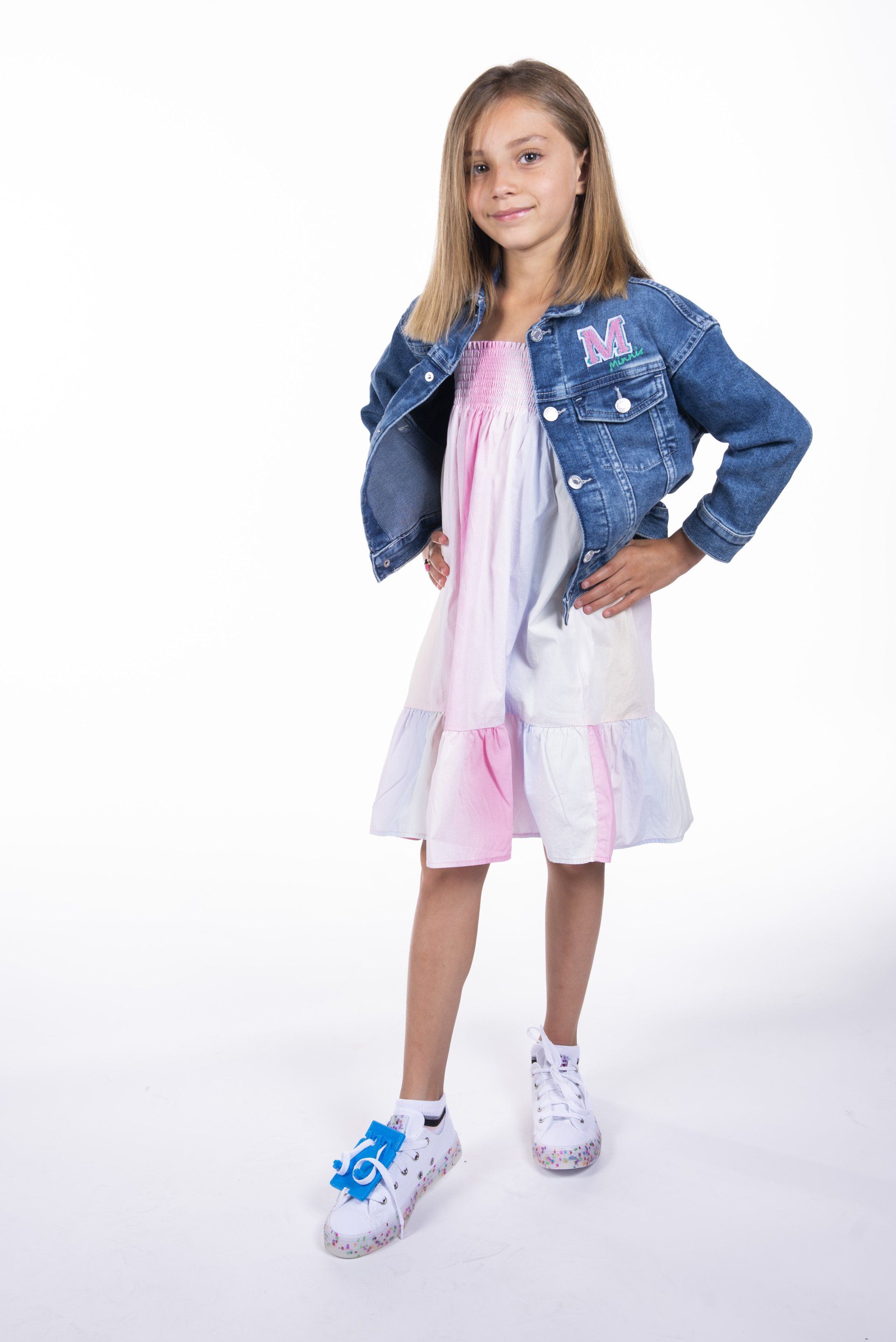 A little girl is wearing a denim jacket and a white dress.